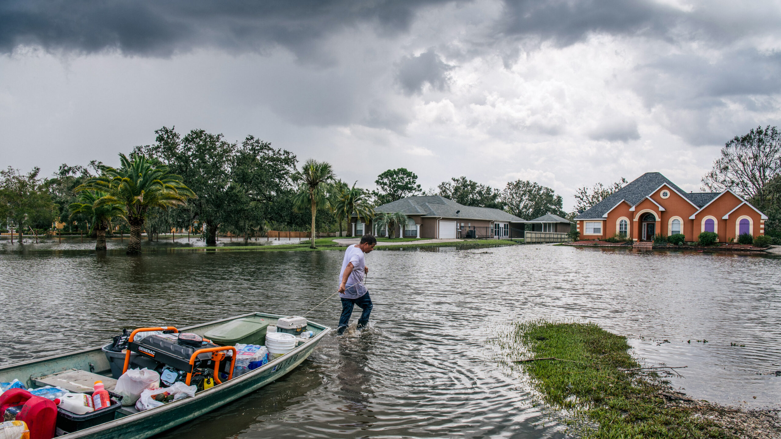 A man pulls a boat through a flooded neighborhood