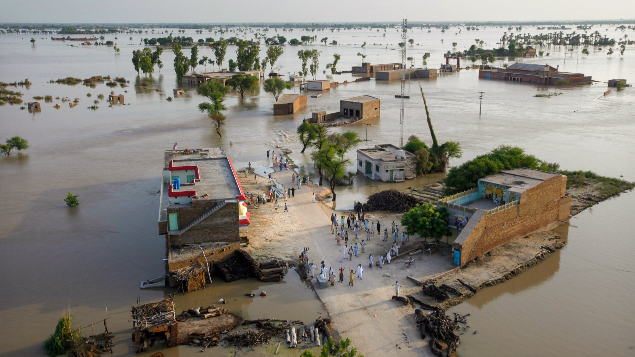 wide shot from a helicopter of a flooded village in Pakistan. Stranded people wave for help from a dry area.