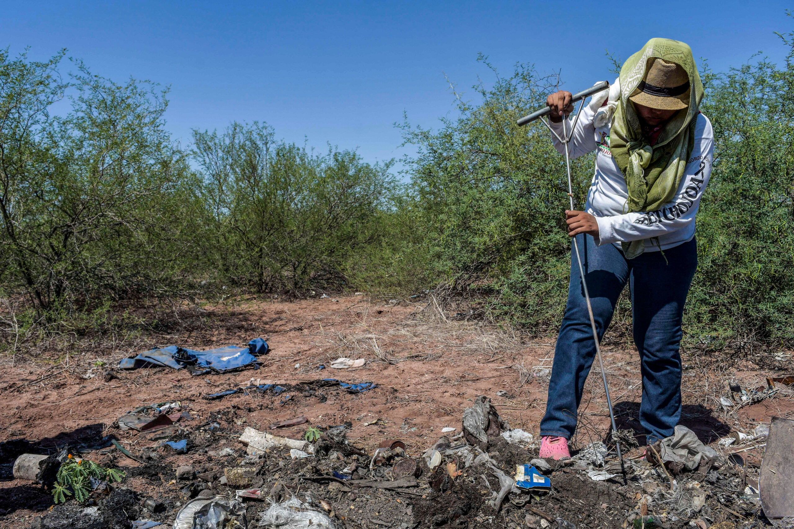 Woman pokes at a pile of burned material on the ground looking for the remains of missing persons.