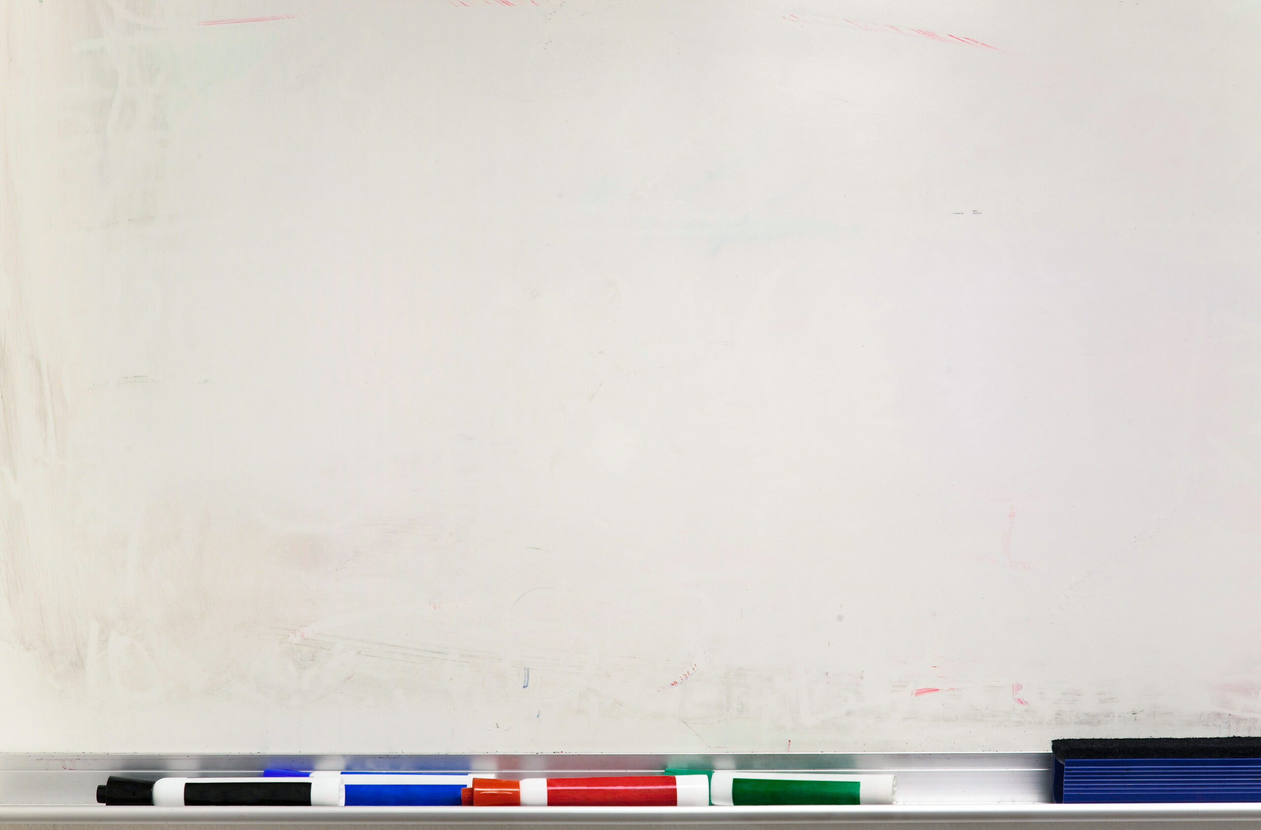 An old empty whiteboard with markers and eraser