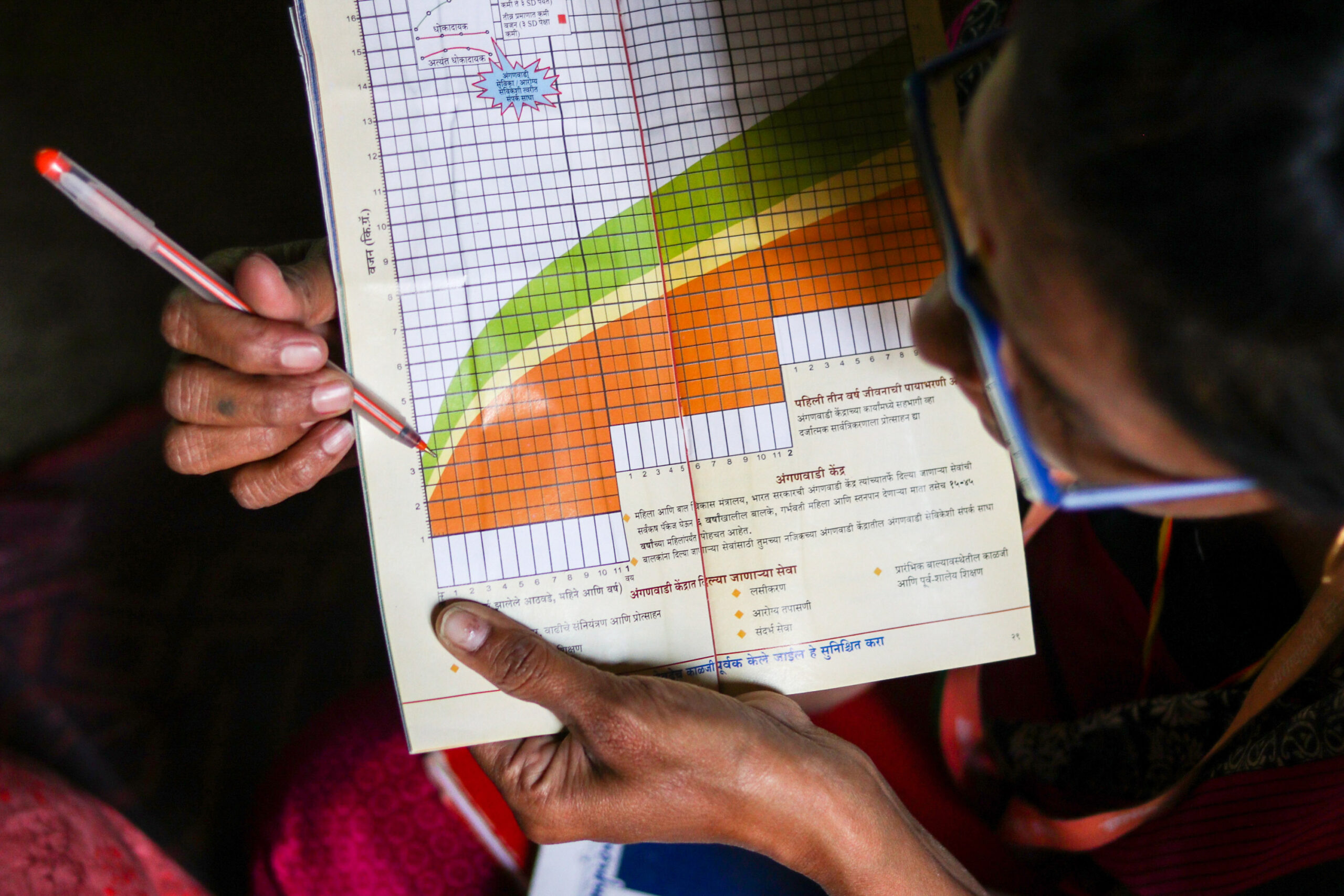 close up of Maya using a pen to point at infant mortality statistics on a leaflet