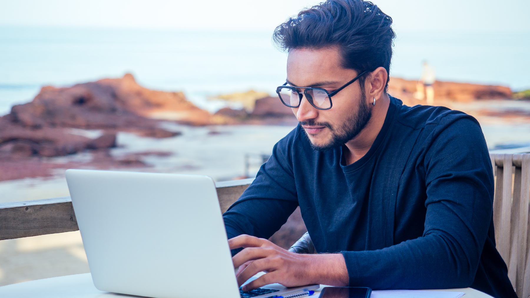 Stock image of a gentleman working at a laptop by the sea.