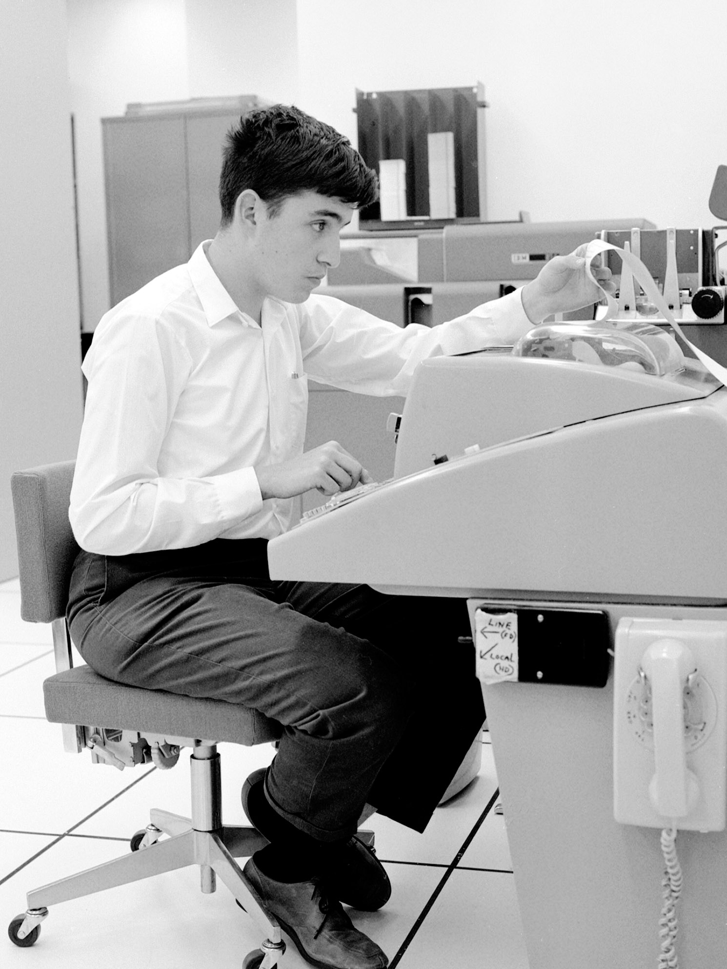 Student looks at paper tape coming from his workstation in the computation center at Darmouth