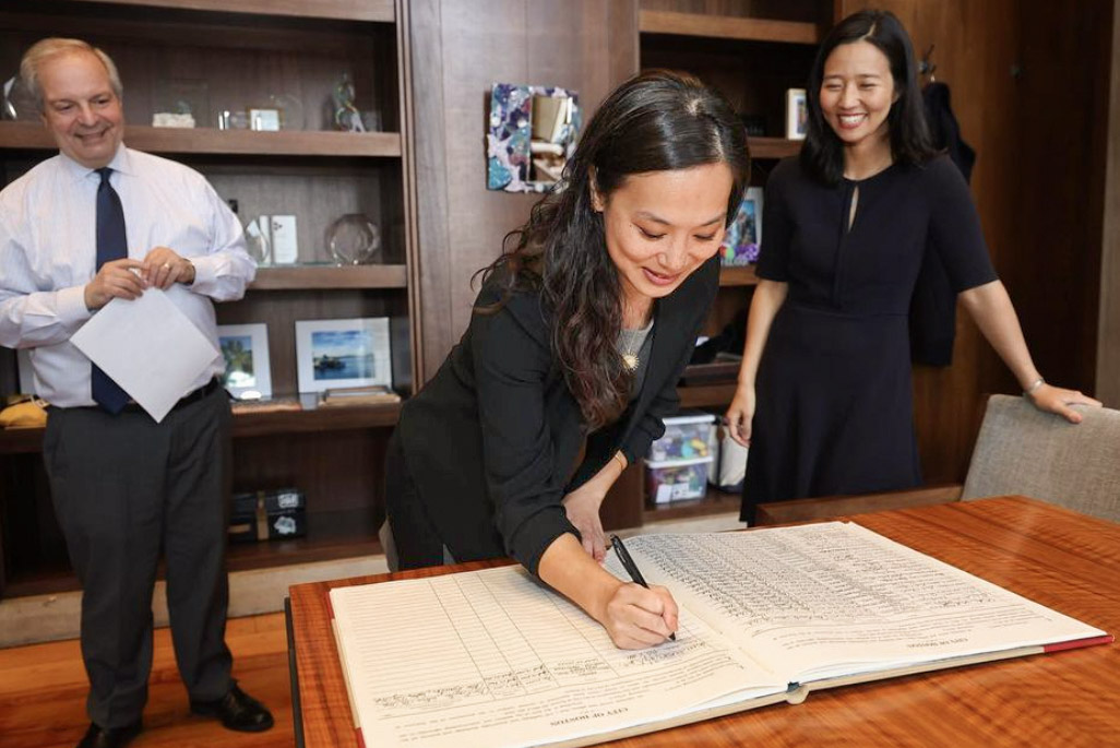 Chu signs a ledger as two people look on
