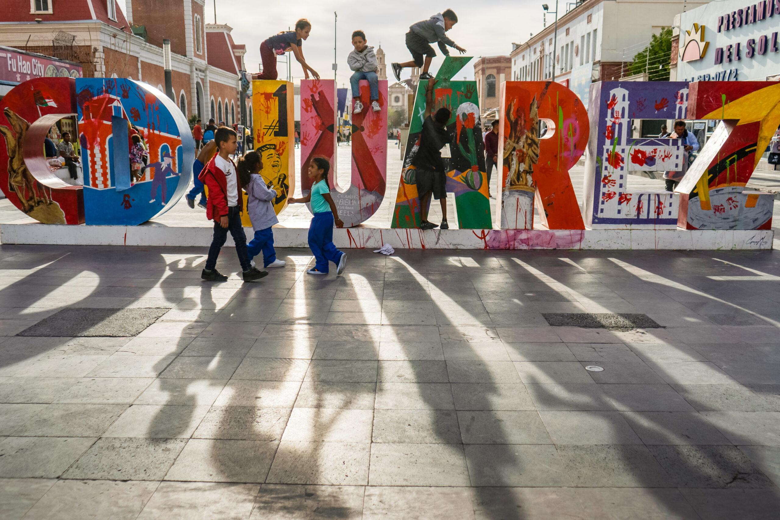 children climb on a 3 dimensional sculpture of the work Juarez.  The sun make long shadows into the foreground.