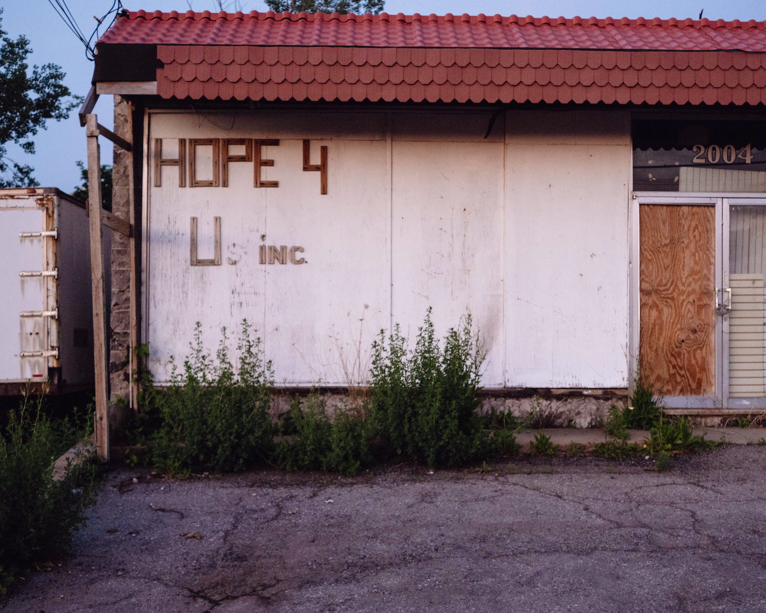 An abandoned building with the words "Hope 4 U inc" on the facade. The doors are boarded up with plywood.