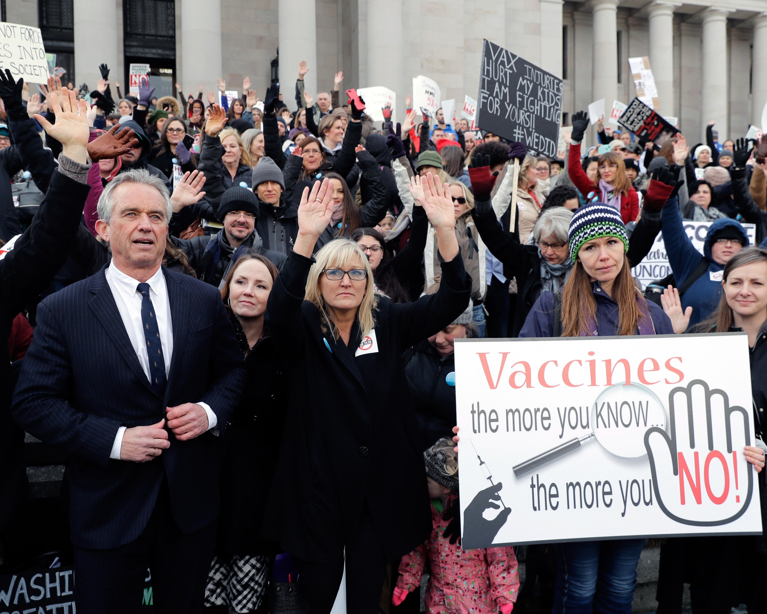 Robert Kennedy Jr. at the Washington state capitol among a group of anti-vax protestors. Sign in the foreground reads, " Vaccines the more you Know...the more you No!"