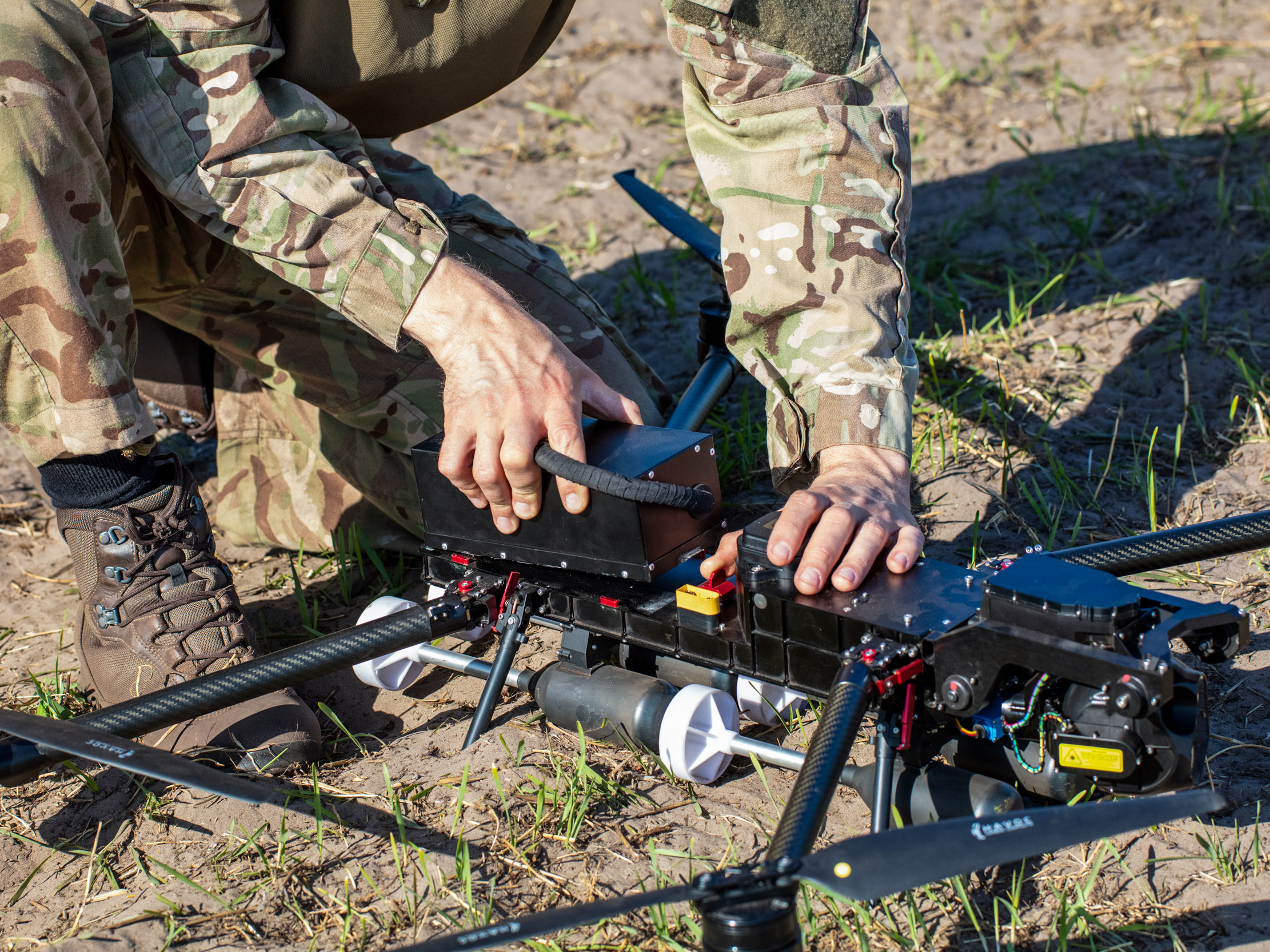 a soldier's hands as he kneels on the ground to assemble a UAV