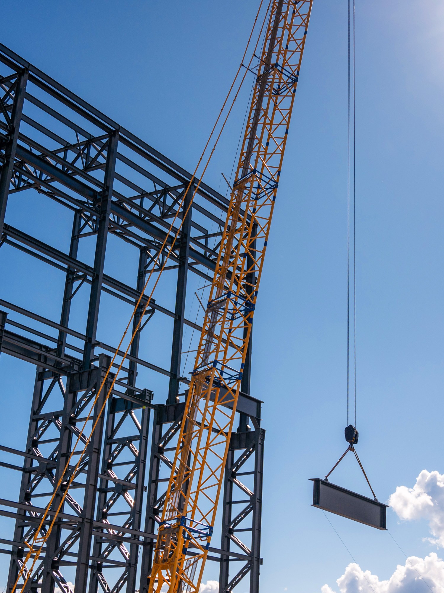 crane hoisting an i-beam  next to a steel building frame