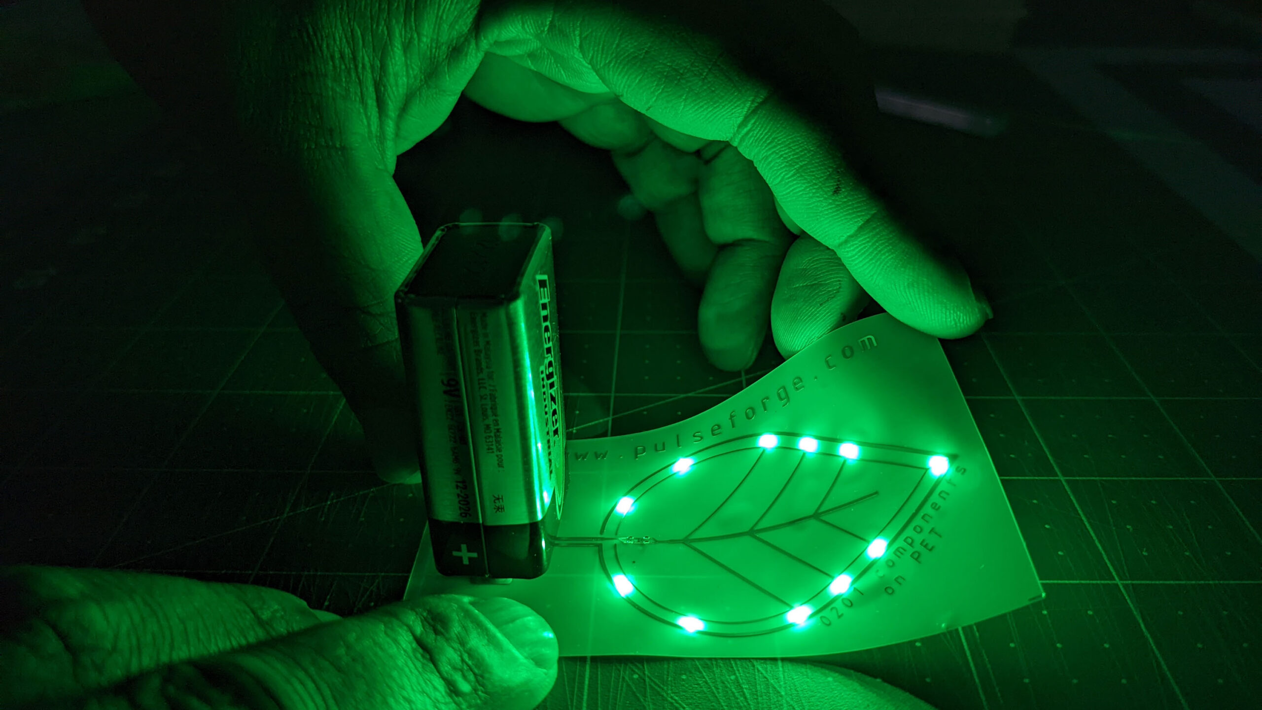 hands hold a print; glowing green LEDs form the outline of a leaf-shape.