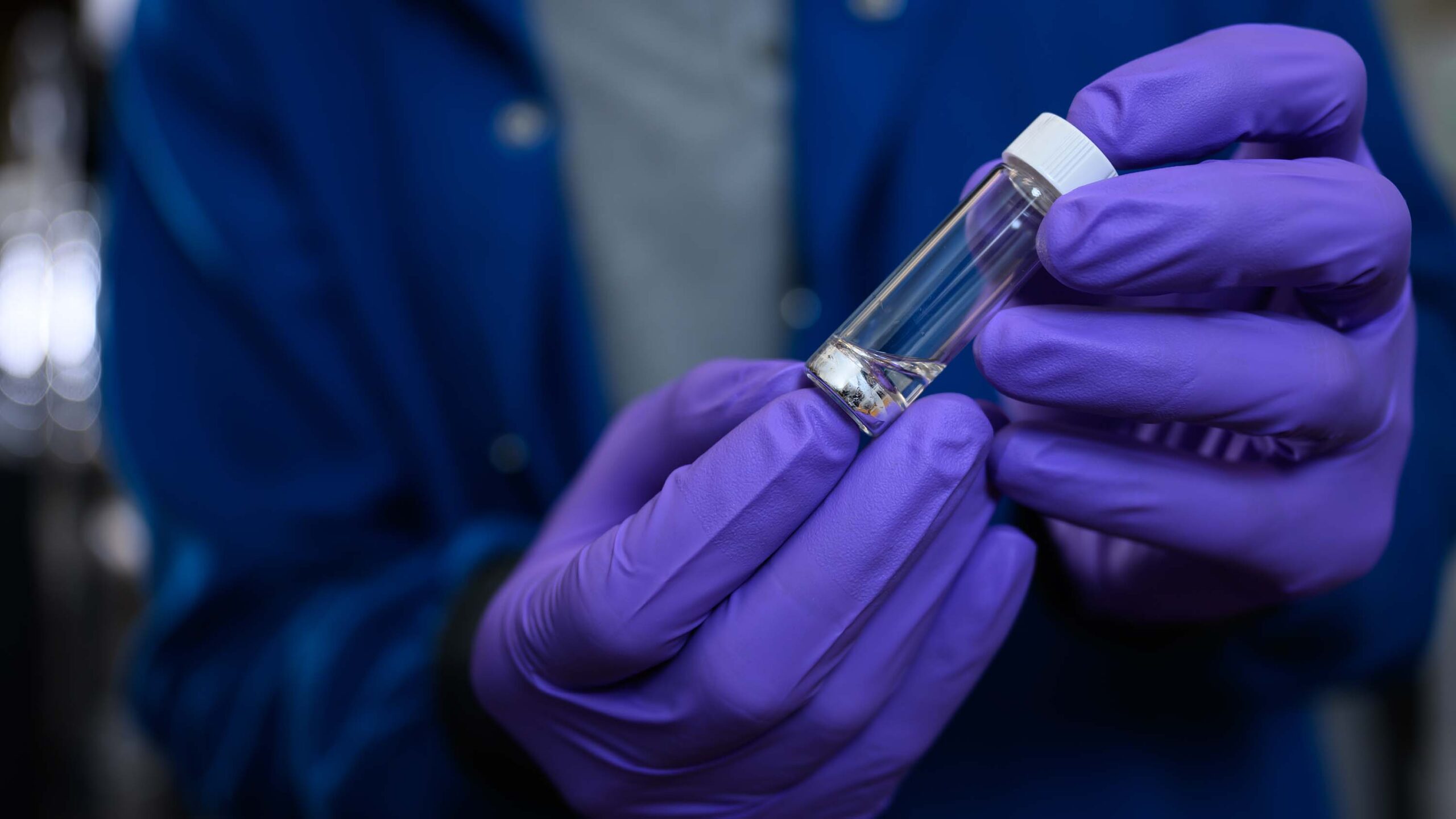 Gloved hands holding a small vial of sodium metal.