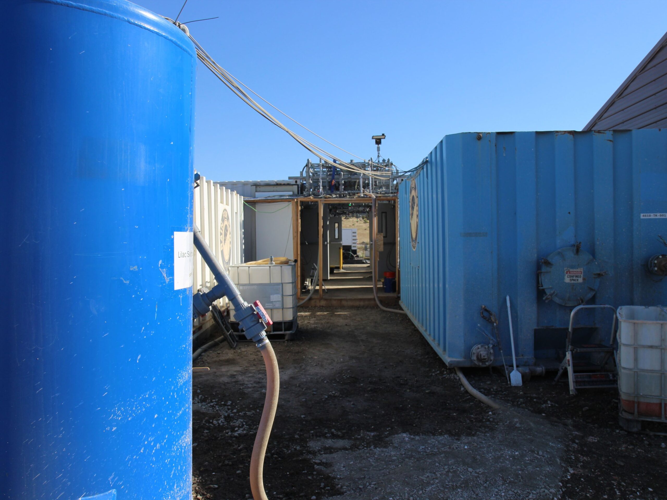 walking path between several tall blue tanks connected by hose